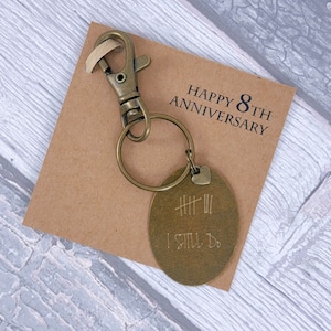 May include: A bronze keychain with a round tag that says "I Still Do" with eight hash marks above the text. The keychain is on a brown card with the text "Happy 8th Anniversary".