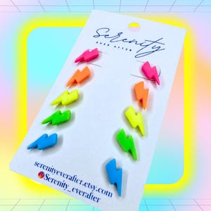 May include: A white display card featuring five pairs of neon lightning bolt earrings in pink, orange, yellow, green, and blue. The card displays the text Serenity Ever After at the top and serenityeverafter.etsy.com Serenity_everafter at the bottom.