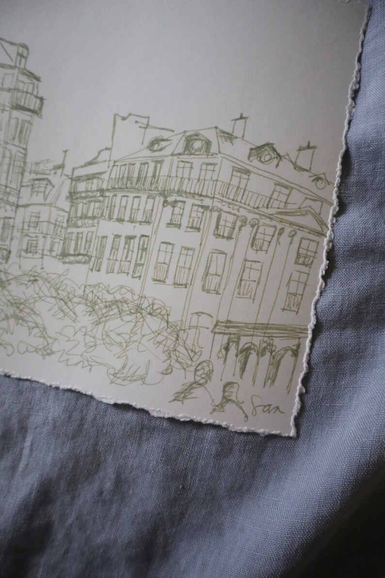 May include: A sketch of a European cityscape with buildings and architectural details. The artwork is rendered in a light green ink on a textured, torn-edge paper. The artist's signature is visible in the lower right corner.