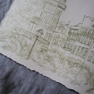 May include: A sketch of a European city scene, featuring buildings with balconies and a street lamp. The artwork is rendered in green ink on a textured, off-white paper with a torn edge. The drawing style is loose and impressionistic.