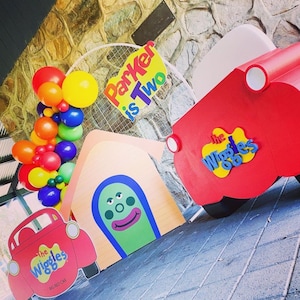 K&ouml;nnte beinhalten: Ein Geburtstags-Party-Setup mit einem roten und gelben 'The Wiggles'-Auto, einem roten und wei&szlig;en 'The Wiggles'-Schild, einem gelben und roten 'Parker is Two'-Schild und einem wei&szlig;en Ballonbogen mit roten, gelben, orangen und gr&uuml;nen Ballons.