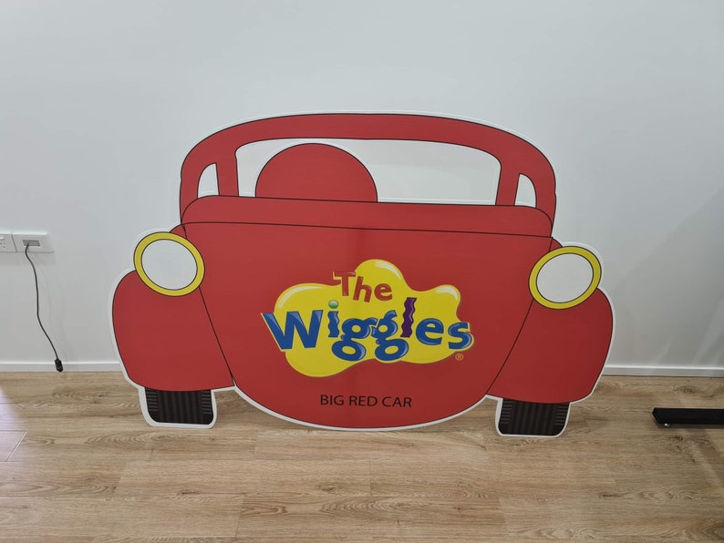 K&ouml;nnte beinhalten: Ein roter Papp-Ausschnitt eines Autos mit den Worten "The Wiggles" und "Big Red Car" darauf.