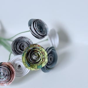 May include: A bouquet of handmade paper flowers. The flowers are made from rolled paper, with a variety of colors and patterns, including map designs. The stems are green and tied with twine.