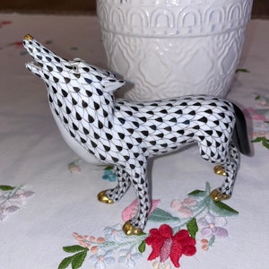 May include: A black and white porcelain wolf figurine with gold accents. The wolf is standing on all four legs with its head tilted back and mouth open. The figurine is decorated with a pattern of black teardrop shapes on a white background.
