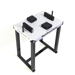 Op de afbeelding: Een witte armworsteltafel met zwarte armleuningen en een zwarte basis. De tafel heeft een honingraatpatroon en de tekst "MagicDragonMaker" gedrukt op de zijkant.