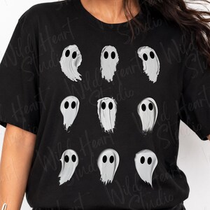 May include: A black short-sleeved t-shirt featuring a graphic print of nine individual white ghosts arranged in a three-by-three grid. Each ghost is depicted with a simple, flowing shape and two solid black oval eyes, creating a repeating pattern.