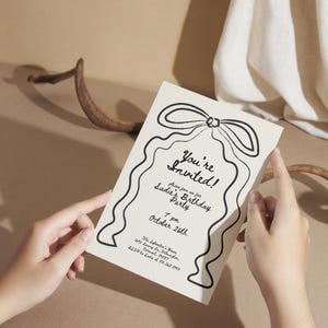 May include: A cream-colored invitation card with black text and a decorative bow design. The card reads "You're Invited!" and announces a birthday party for Sadie on October 26th at 7 pm. The card also includes the party's address.