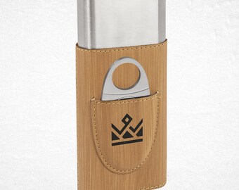 Puede incluir: Un estuche para puros con una parte superior de acero inoxidable y un cuerpo de cuero sintético de color beige. Un cortador de puros plateado está en el bolsillo delantero. El bolsillo tiene un logotipo de corona negra.