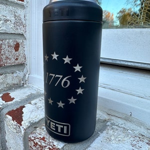 May include: Black YETI Rambler 12 oz. can insulator with a silver 1776 and a circle of stars around it.