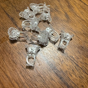 May include: A pile of clear plastic clips with a decorative design. The clips are used to hold curtains or drapes.