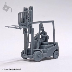 May include: A gray plastic model of a forklift with a driver figure. The forklift has a raised platform and a set of forks. The model is in N scale.