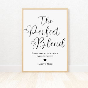 Op de afbeelding: Een wit bord met zwarte tekst die "The Perfect Blend" en "Please take a favor of our favorite coffee!" luidt, met een zwart hart en de namen "Hailey & Mark" eronder. Het bord is ingelijst in een licht houten frame.