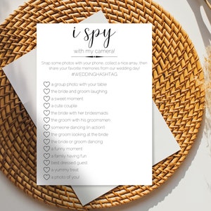 Può includere: Un biglietto bianco con il testo "i spy with my camera!" e un elenco di cose da fotografare a un matrimonio, come "una foto di gruppo con il tuo tavolo", "la sposa e lo sposo che ridono" e "una foto di te!"