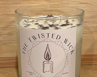 Puede incluir: Una vela blanca con una etiqueta en blanco y negro que dice "The Twisted Wick Candle Co. 2020". La vela está en un tarro de vidrio transparente y tiene una cera blanca con cristales morados.