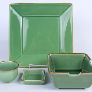 May include: A set of four green ceramic dishes with brown rims. The set includes a large square plate, a smaller square dish, a round bowl, and a square bowl with a handle.