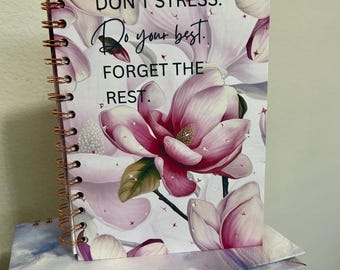 May include: A pink and white spiral bound journal with a floral design and the text "DON'T STRESS. Do your best. FORGET THE REST."