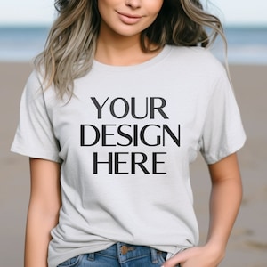 May include: A white t-shirt with short sleeves and a crew neck. The shirt has the text "YOUR DESIGN HERE" printed on the front in black.