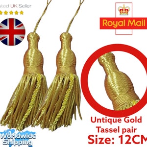 May include: Two gold tassels, each with a woven top and a fringe of threads. The tassels are approximately 12 cm in length. The image includes a close-up of one tassel and text that reads "Unique Gold Tassel pair".