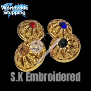 Könnte beinhalten: Vier goldfarbene, verzierte Knöpfe mit juwelenfarbenen Zentren: rot, blau, grün und braun. Die Knöpfe haben ein detailliertes, durchbrochenes Design. Der Text "S.K Embroidered" steht unten und "Worldwide Shipping" oben.
