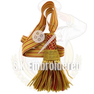 Peut inclure: Un gland décoratif aux couleurs or et rouge. Il présente une bande dorée tissée avec des rayures rouges, un centre en filet rouge et un gland or et rouge. Le texte "S.K Embroidered" est visible.