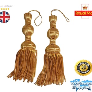 May include: A pair of gold decorative tassels, featuring a spherical design and long, flowing fringe. The tassels are made from a shiny, woven material and are suspended by a thin, matching cord. These elegant tassels are suitable for home decor.