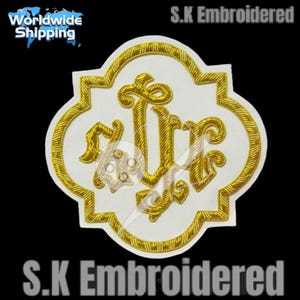 May include: Embroidered patch with a white background and a gold-colored, ornate design. The design features stylized letters and decorative elements within a quatrefoil shape. The patch is bordered with gold thread and the text "S.K Embroidered" is visible.