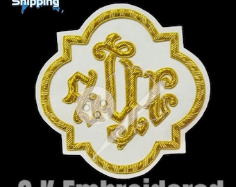 May include: Embroidered patch with a white background and a gold-colored, ornate design. The design features stylized letters and decorative elements within a quatrefoil shape. The patch is bordered with gold thread and the text "S.K Embroidered" is visible.