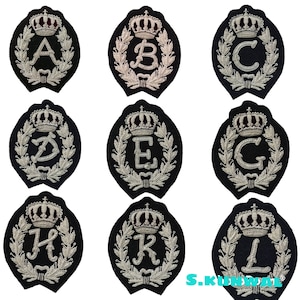 Könnte beinhalten: Neun gestickte Patches mit schwarzem Hintergrund, silbernem Faden und einer Krone über jedem Buchstaben. Die Buchstaben sind A, B, C, D, E, F, G, H und I.