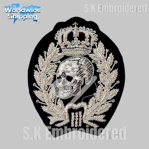 Könnte beinhalten: Schwarzer, gestickter Aufnäher mit Totenkopf-, Kronen- und Lorbeerkranz-Design. Der Totenkopf ist mit silberfarbenem Faden detailliert. Der Aufnäher trägt den Text "S.K Embroidered" und "Worldwide Shipping".