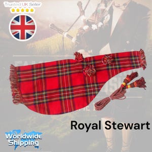 May include: A red Royal Stewart tartan bagpipe bag with yellow and green plaid lines. The bag has three decorative pom-poms and a fringe along the edge. A rope with tassels is attached. The text "Royal Stewart" is visible.