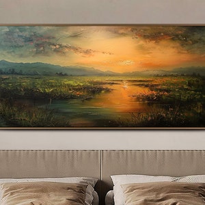 May include: A painting of a landscape with a lake, mountains, and a sunset. The sky is a mix of orange, pink, and purple. The lake is a deep blue and reflects the colors of the sky. The mountains are a dark green and are in the background. The painting is framed in a brown frame.