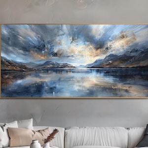 May include: A framed landscape painting shows a tranquil lake scene under a dramatic sky. The artwork features a gold frame and a palette of blues, greys, and golds. It hangs above a white sofa and a round wooden coffee table, creating a calming atmosphere.