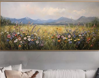 May include: A framed landscape oil painting depicts a vibrant wildflower meadow with colorful blooms, set against a backdrop of rolling hills and a cloudy sky. The artwork is displayed above a white sofa and a wooden coffee table.