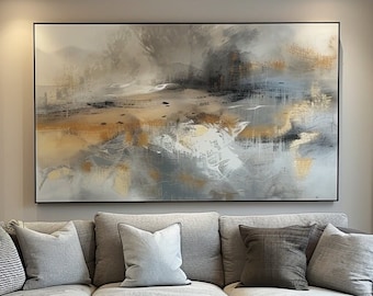 May include: A large rectangular abstract painting featuring blended strokes of gray, white, and metallic gold tones hangs above a light gray sectional sofa. The sofa is adorned with several throw pillows in shades of gray and black, and a gray tray sits on the chaise.