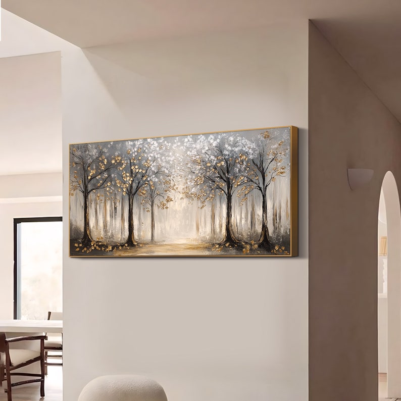May include: A rectangular wall art painting featuring a forest scene with dark tree trunks, white foliage, and metallic gold leaf accents. The artwork is set within a thin gold frame and depicts a light-filled path between the trees.