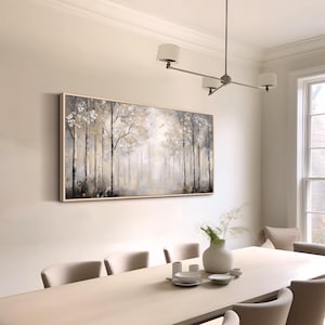 May include: A framed abstract painting of a forest scene in shades of gray, white, and gold. The painting is hanging on a white wall in a dining room with a white table and chairs.