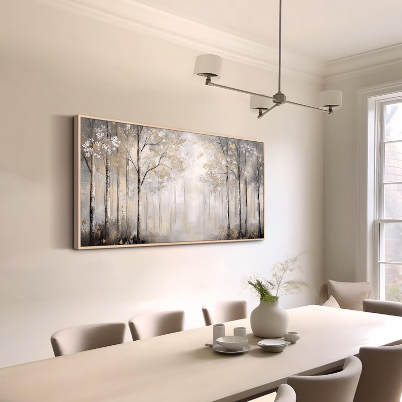 May include: A framed abstract painting of a forest scene in shades of gray, white, and gold. The painting is hanging on a white wall in a dining room with a white table and chairs.