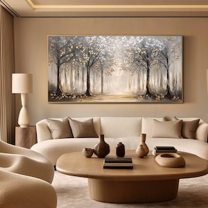May include: A large rectangular wall art piece featuring a forest landscape with dark tree trunks, white foliage, and metallic gold leaf accents. The painting is framed in a thin gold border and depicts a light-filled path through the trees.