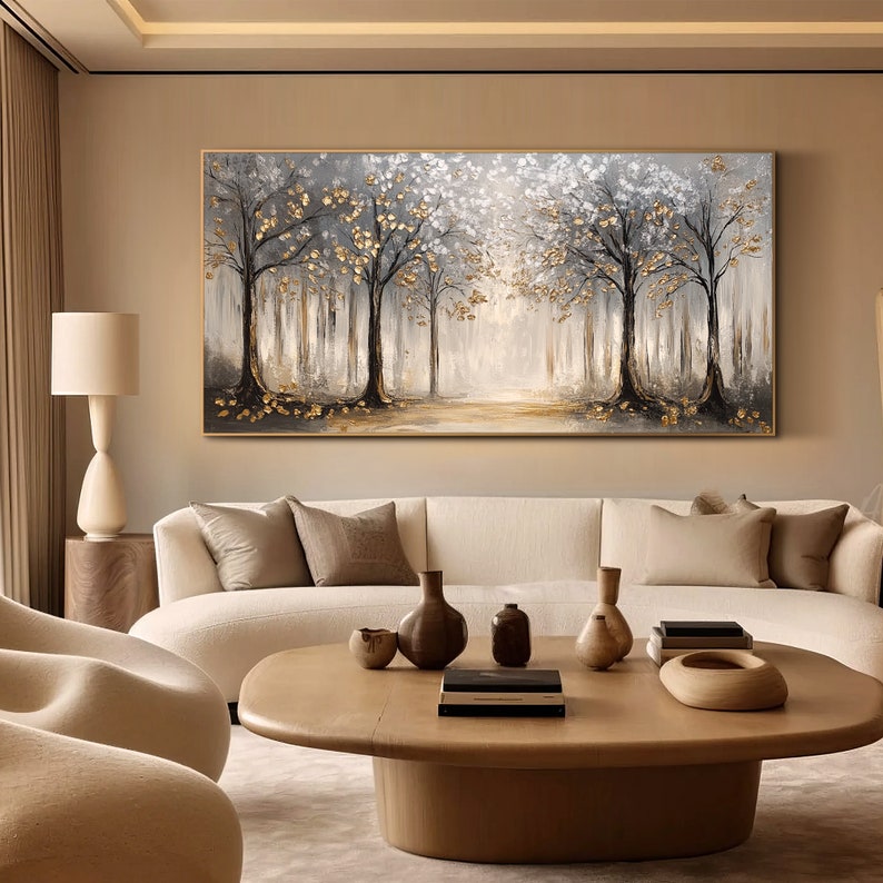 May include: A large rectangular wall art piece featuring a forest landscape with dark tree trunks, white foliage, and metallic gold leaf accents. The painting is framed in a thin gold border and depicts a light-filled path through the trees.