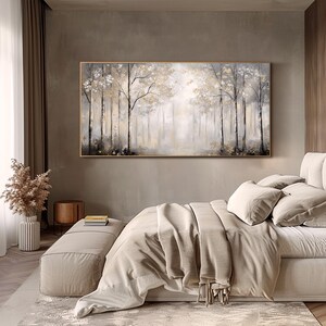 May include: A large abstract painting of a forest scene in shades of gray and white. The painting is framed in a gold frame and hangs above a bed with a beige duvet cover.