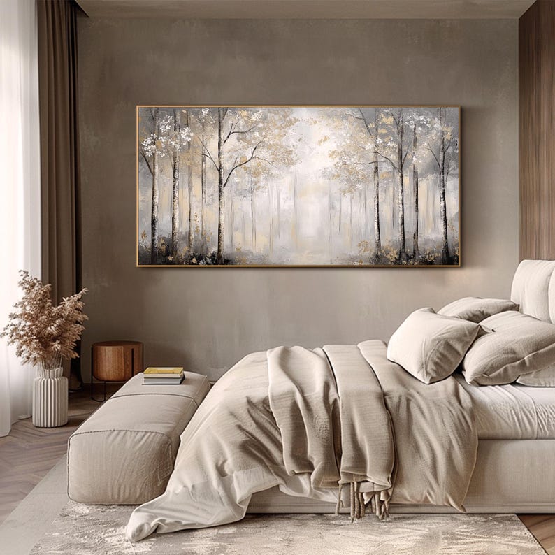 May include: A large abstract painting of a forest scene in shades of gray and white. The painting is framed in a gold frame and hangs above a bed with a beige duvet cover.