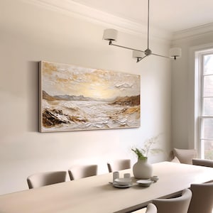 May include: A large rectangular landscape painting featuring a textured impasto technique in shades of white, cream, gold, and brown. The artwork depicts a serene coastal scene with rolling hills, a calm body of water, and a bright, glowing sky.