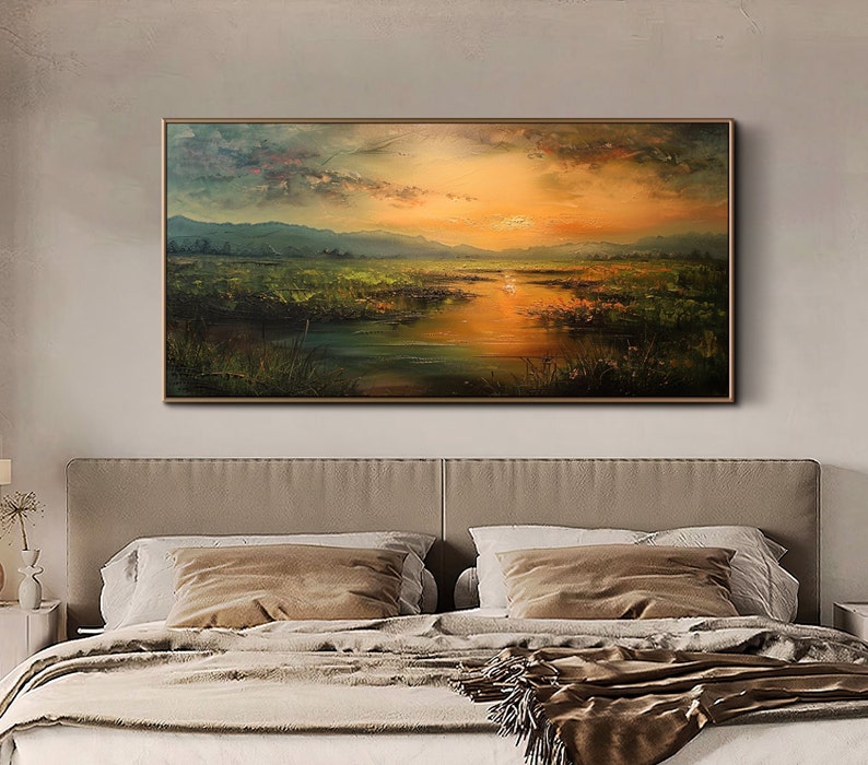 May include: A painting of a landscape with a lake, mountains, and a sunset. The sky is a mix of orange, pink, and purple. The lake is a deep blue and reflects the colors of the sky. The mountains are a dark green and are in the background. The painting is framed in a brown frame.