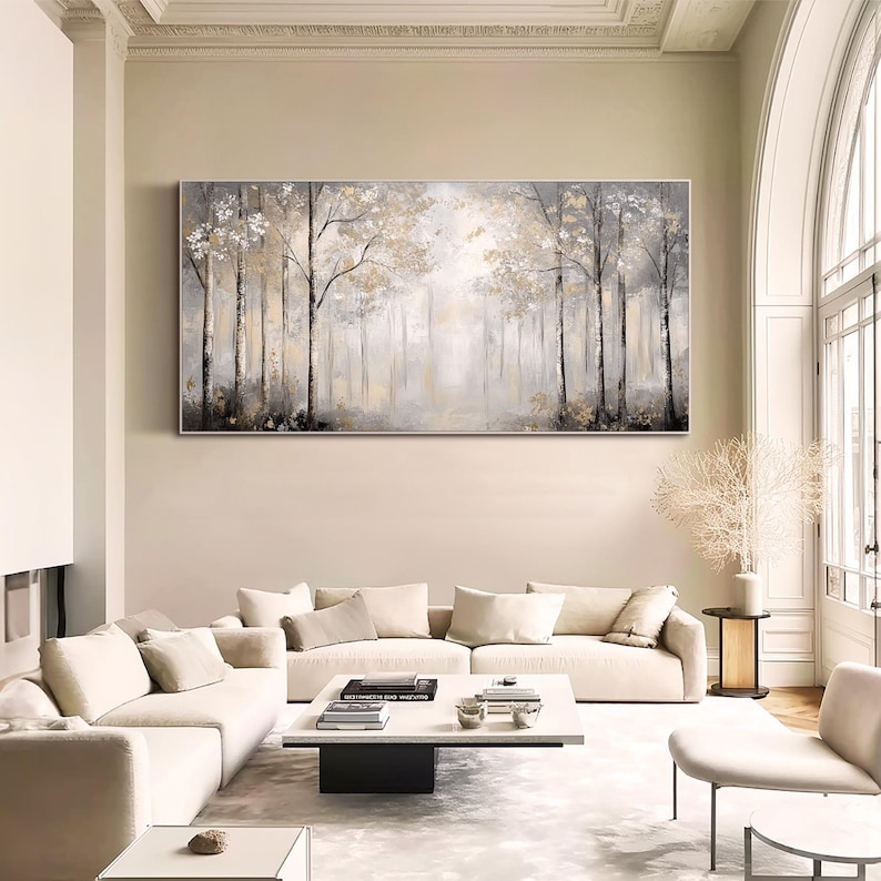 May include: A large, horizontal canvas painting depicting a misty forest scene with tall, slender trees in shades of gray and gold. The painting is hung on a wall in a modern living room setting.