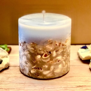 May include: A blue and white candle with seashells embedded in the wax. The candle is cylindrical and has a smooth, polished finish.