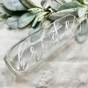 Op de afbeelding: Een heldere glazen champagnefluit met het woord "bride" in wit schrift aan de zijkant.