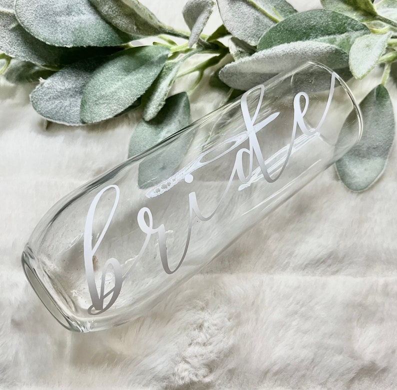 Op de afbeelding: Een heldere glazen champagnefluit met het woord "bride" in wit schrift aan de zijkant.