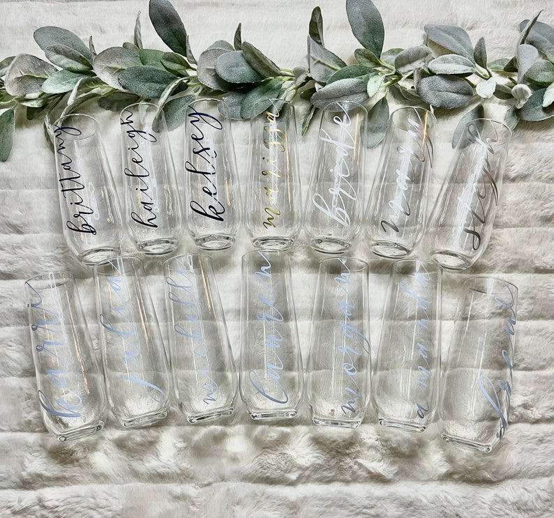 Op de afbeelding: Een set van 14 heldere glazen champagnefluiten met gepersonaliseerde kalligrafie namen. De namen zijn geschreven in zwarte en zilveren inkt.