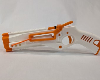 May include: A white and orange toy gun with a black elastic band. The gun has a trigger, a safety, and a barrel. The gun is made of plastic.