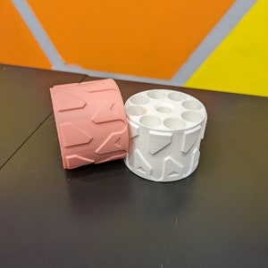 May include: Two round containers with a textured design. One container is pink and the other is white.